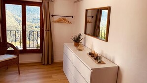 Una stanza con pavimento in legno, una cassettiera bianca, uno specchio, una pianta e una sedia.