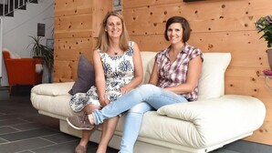 Two people sitting on a sofa in a room with a wooden wall and a staircase in the background. - Panorama Ischgl in Kappl by Interhome (Kappl)