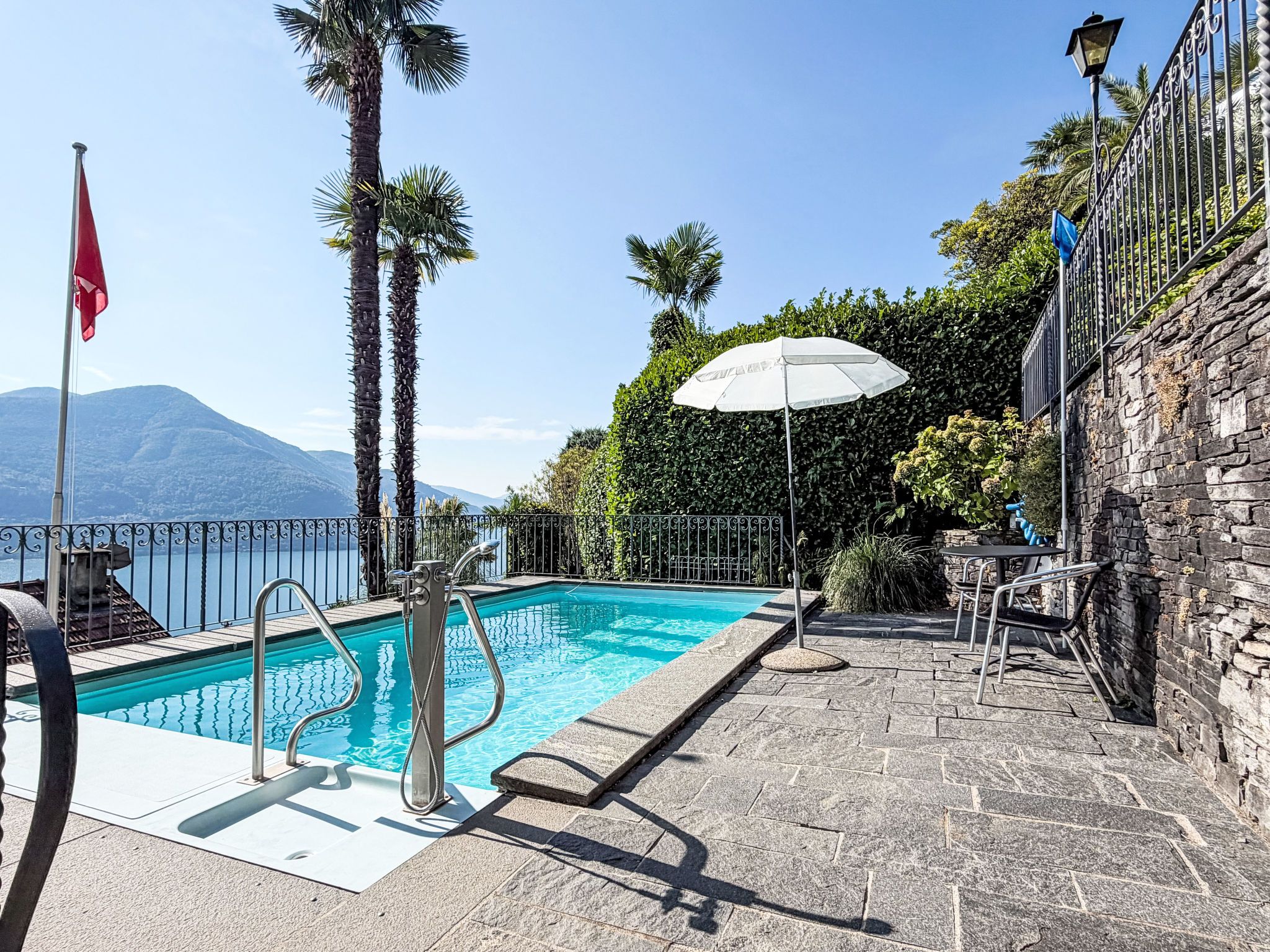 A swimming pool with a view of mountains, a flag, and a stone wall.