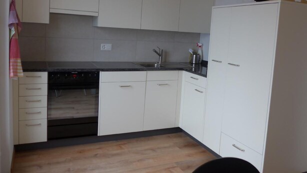 A kitchen with white cabinets, a black countertop, and a wooden floor. - Casa Ninfea by Interhome (Brissago)
