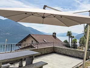 Una terraza con una mesa y una sombrilla, con vistas a un lago y montañas.