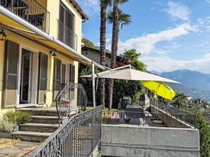 A two-story building with a balcony, outdoor seating, and a mountain view. - Casa Ninfea by Interhome (Brissago)