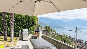 An outdoor patio with a stone table and benches, a grill, and a view of a lake and mountains. - Casa Ninfea by Interhome (Brissago)