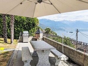 An outdoor patio with a stone table and benches, a grill, and a view of a lake and mountains. - Casa Ninfea by Interhome (Brissago)