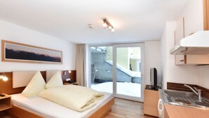 Een moderne hotelkamer met een groot bed, een kitchenette en een schuifdeur naar een besneeuwde omgeving.