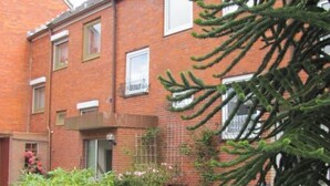 A brick residential building with a small garden area, a pathway, and a large tree. - Wohnung in Altengroden mit Garten by Interhome (Wilhelmshaven)