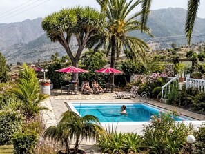 A swimming pool with lounge chairs and umbrellas, surrounded by lush greenery and mountains in the background. - Apartment El Hierro by Interhome (El Paso)