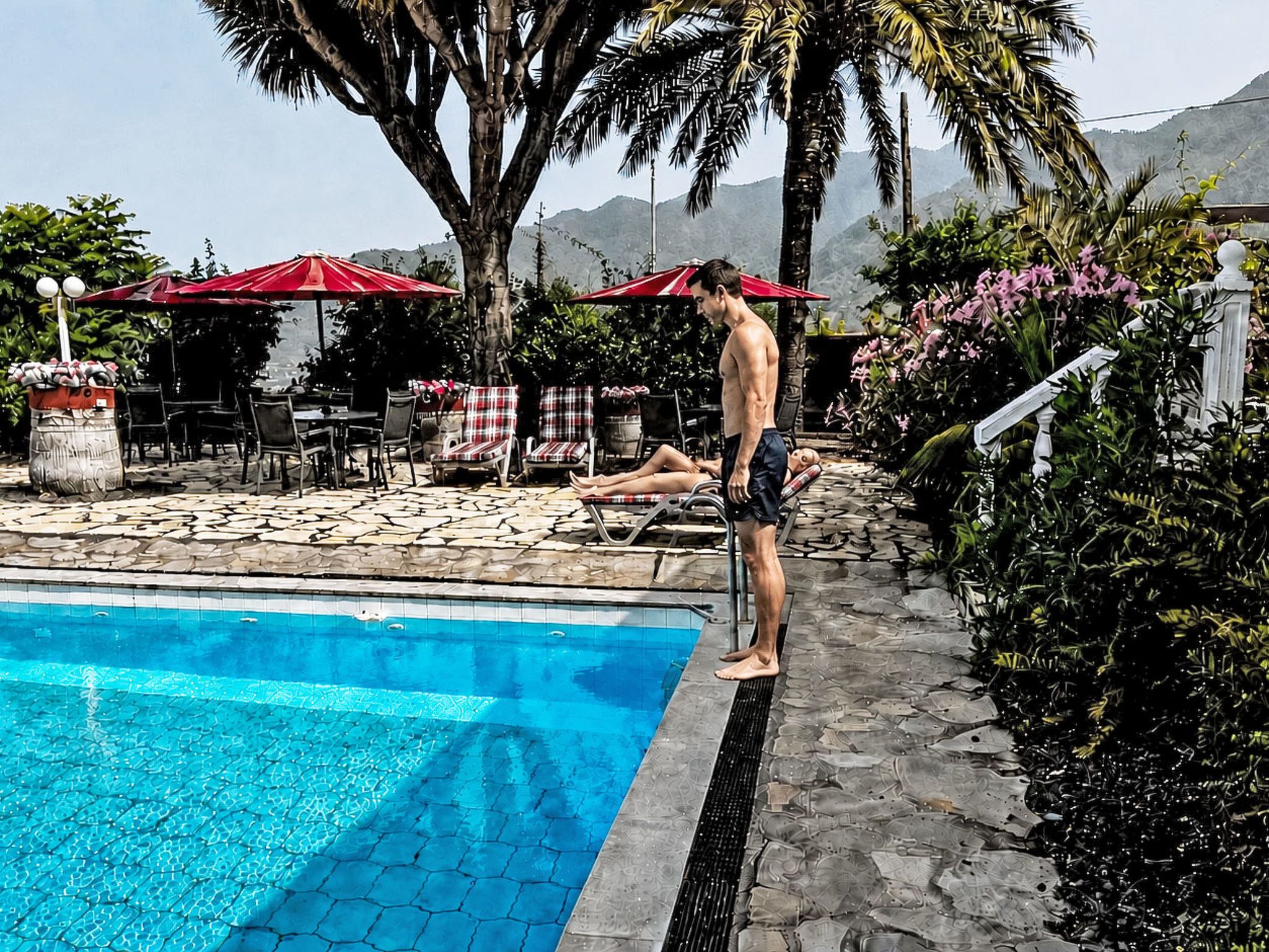 A swimming pool with a tiled edge, surrounded by lounge chairs and red umbrellas.