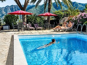 A swimming pool with lounge chairs and umbrellas, surrounded by greenery and mountains. - Apartment El Hierro by Interhome (El Paso)