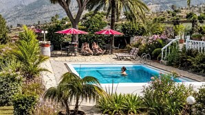 A swimming pool with lounge chairs and umbrellas, surrounded by lush greenery and mountains in the background. - La Gomera by Interhome (El Paso)