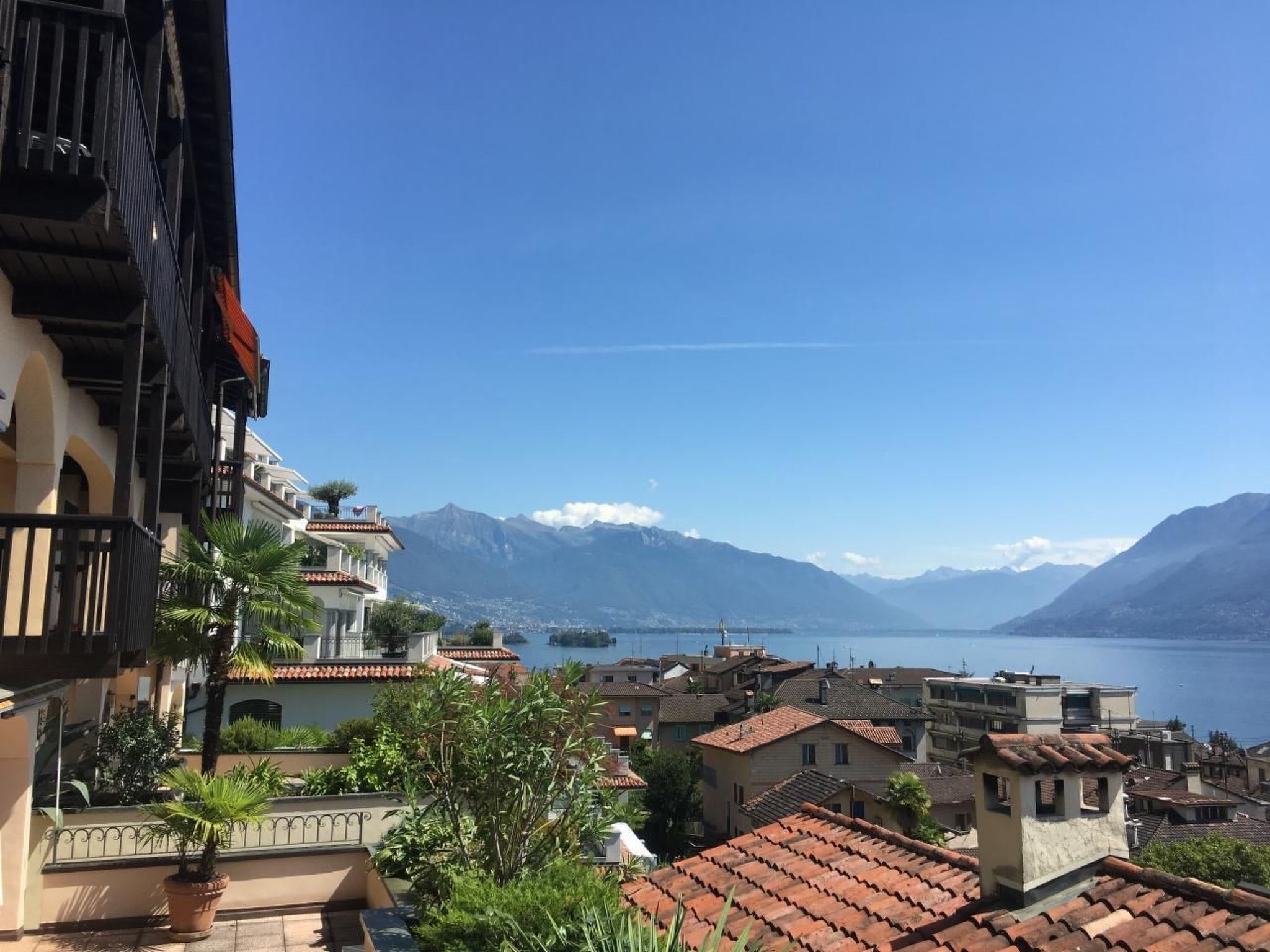 Eine Küstenstadt mit terrakottafarbenen Dächern, blauem Himmel und Bergen im Hintergrund.