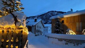 A snow-covered street with houses, a wooden fence with lights, and a mountain in the background. - Chesa Ladina by Interhome (La Punt-Chamues-ch)