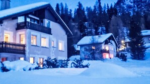 A two-story building with a balcony, surrounded by snow-covered trees and a mountainous backdrop.