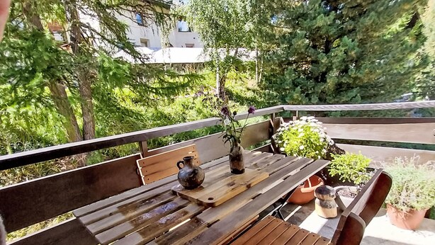 A wooden table with a vase and potted plants on a balcony with a railing.