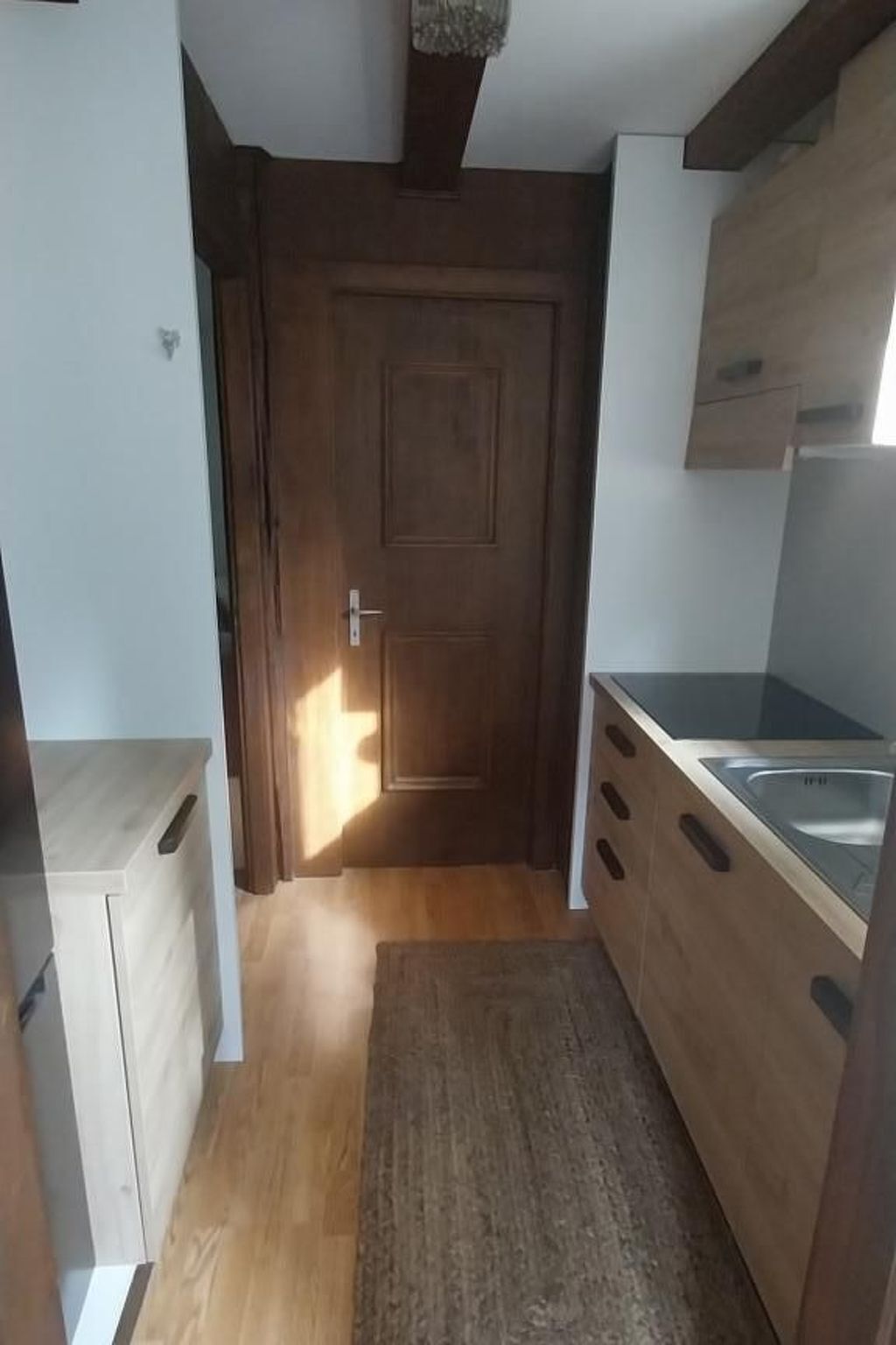 Een smalle keuken met houten kastjes, een inbouwspoelbak en een deur naar een andere kamer.