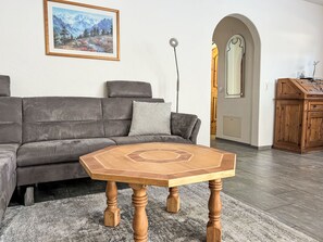 En stue med en hjørnesofa, et sekskantet træbord, et maleri på væggen og et træskab.