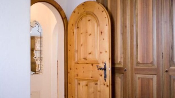 Une porte en bois dotée d’un simple loquet, un miroir au-dessus, et un mur recouvert de panneaux de bois.