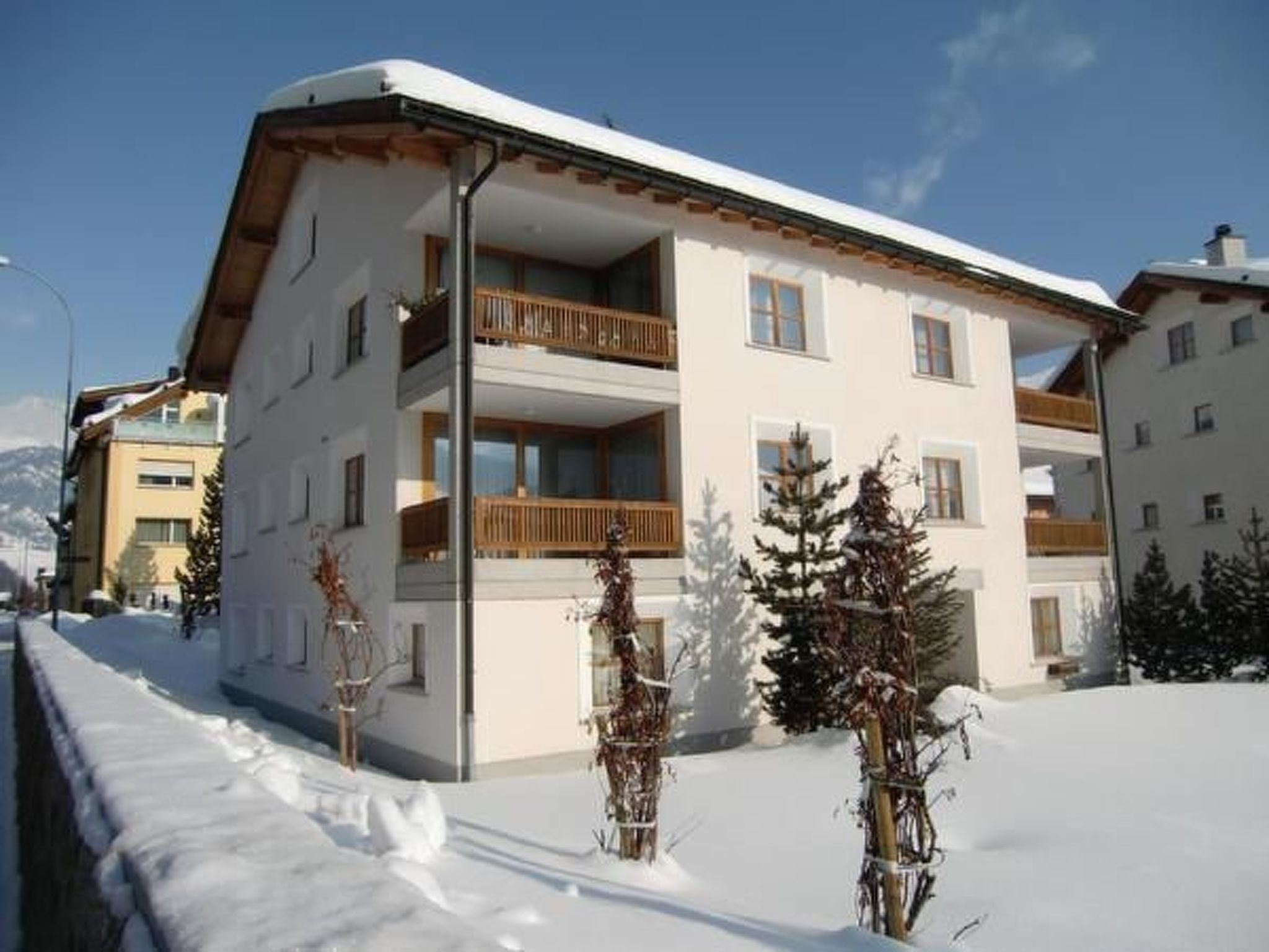 Un edificio de varios pisos con balcones, rodeado de nieve y árboles.