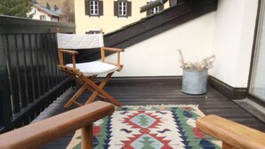 A balcony with a wooden deck, a patterned rug, and a folding chair. - Chesa Maura by Interhome (Celerina)