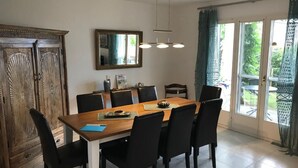 A dining area with a wooden table, black chairs, a chandelier, a mirror, and a view of greenery through the glass door. - Piazzogna by Interhome (Piazzogna)
