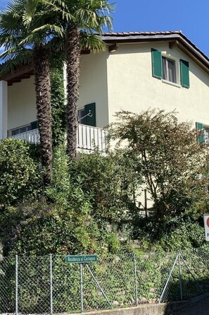 A residential building with a balcony, surrounded by lush greenery and a chain-link fence. - Piazzogna by Interhome (Piazzogna)