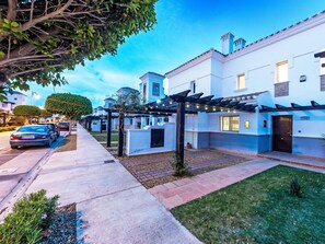 A residential street with white houses, a covered patio area, and a car parked on the side. - "Casa La Torre" mit Wallbox by Interhome (Roldán)