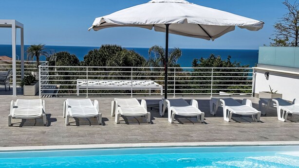 A poolside area with lounge chairs and an umbrella, overlooking a clear blue sea. - Casa Gaetano by Interhome (Balestrate)