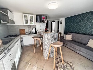 Een moderne keuken met een centraal eiland, barkrukken, een bank en een aan de muur bevestigde televisie.