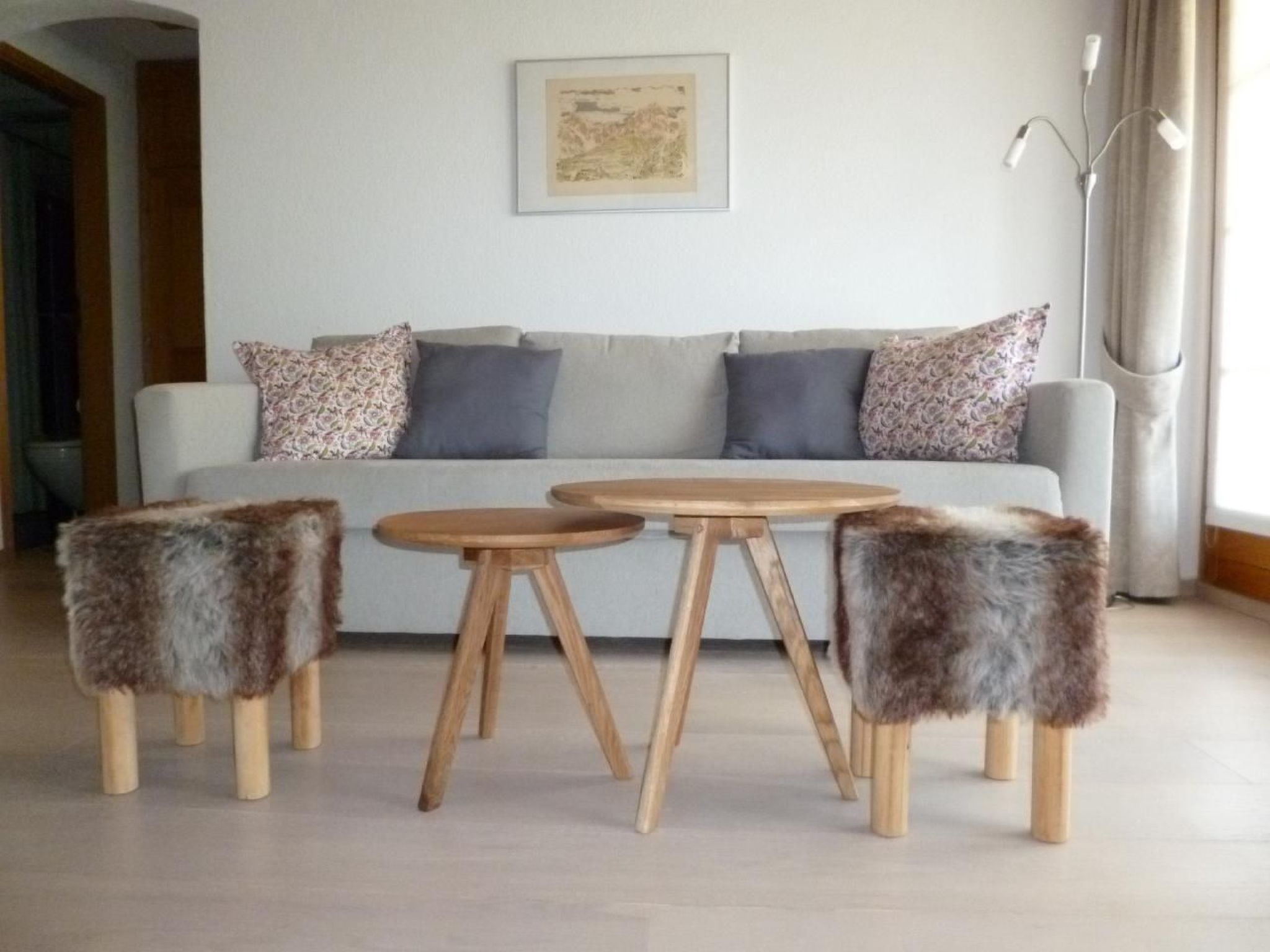Ein Wohnzimmer mit einer Couch, zwei runden Holztischen und drei flauschigen Hocker.