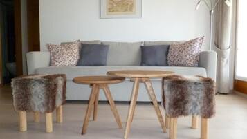 Ein Wohnzimmer mit einer Couch, zwei runden Holztischen und drei flauschigen Hocker.