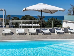 A poolside area with lounge chairs, a white umbrella, and a view of the ocean. - Villetta Cottone in Balestrate by Interhome (Balestrate)