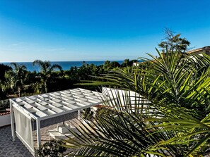 Una terrazza con vista sull'oceano, circondata da palme e da una struttura bianca.
