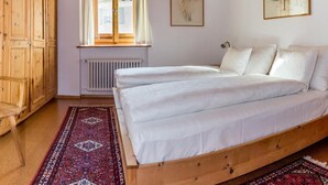 Een slaapkamer met een houten bed, een raam met gordijnen, een radiator en een houten garderobe.