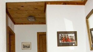 Een gang met houten vloeren, witte muren en een houten plafond. Er hangt een ingelijste foto aan de muur en er staat een houten kast aan de rechterkant.