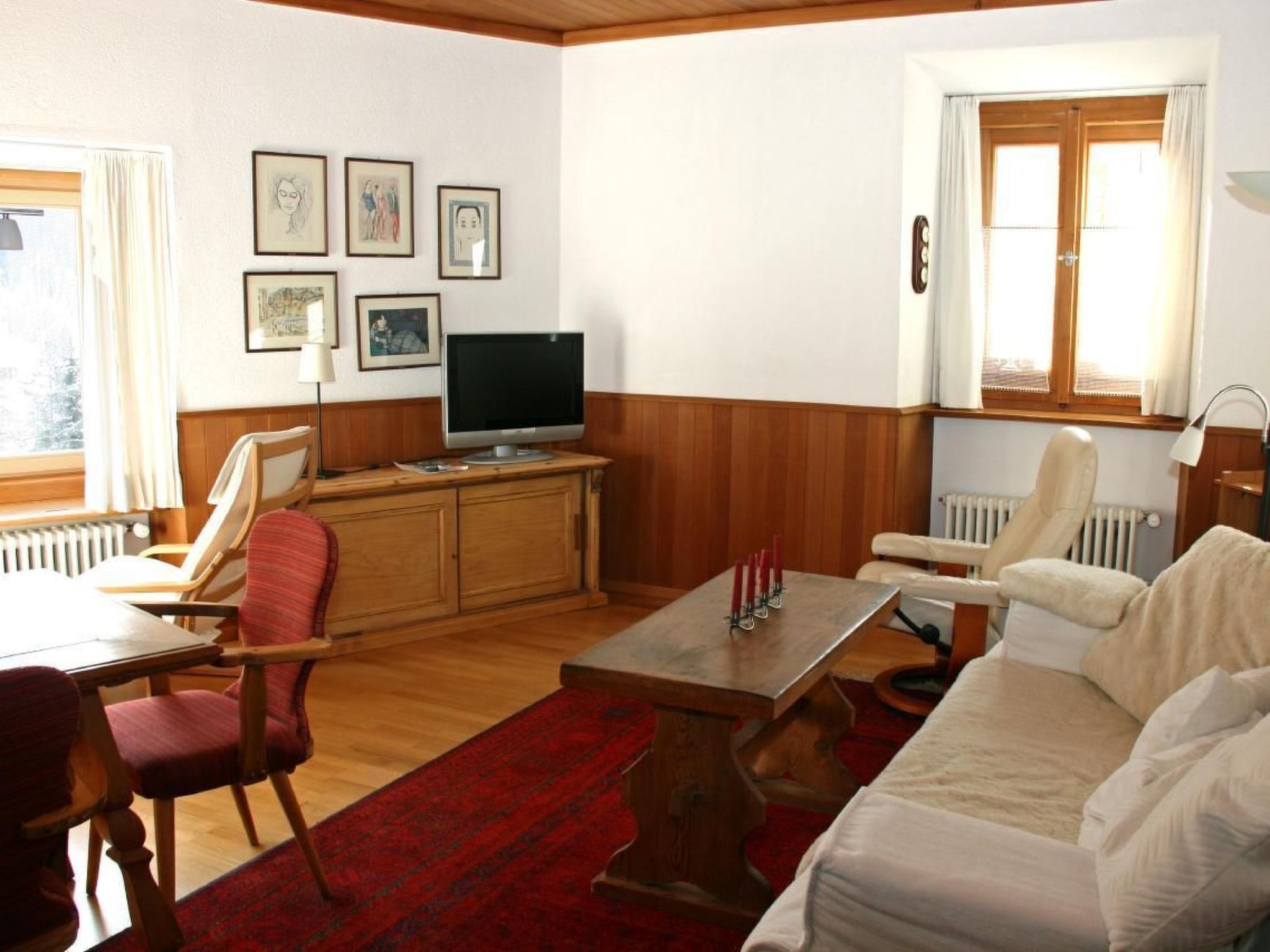 Ein Wohnzimmer mit einem Holzkabinett, einem Fernseher, einem roten Teppich und einem weißen Sofa.