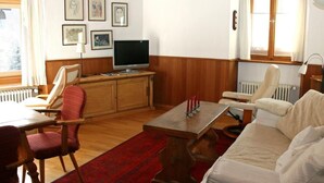 Een woonkamer met een houten kast, een televisie, een rood kleed en een witte bank.