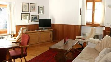 Ein Wohnzimmer mit einem Holzkabinett, einem Fernseher, einem roten Teppich und einem weißen Sofa.