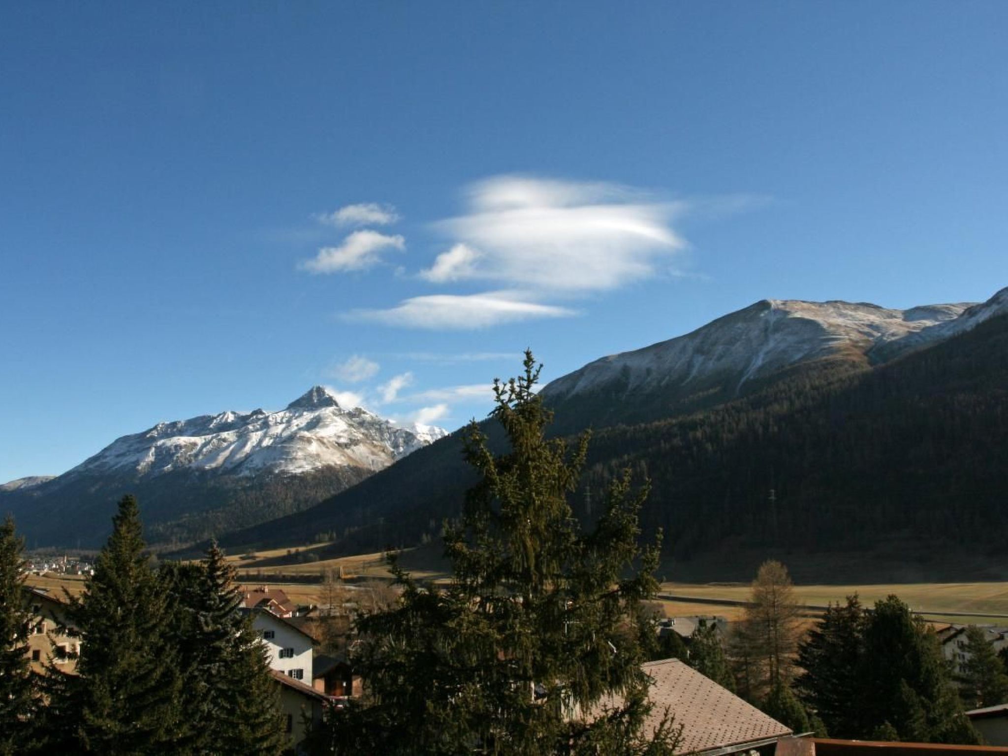 Paisaje montañoso con picos nevados y un valle con casas y árboles.