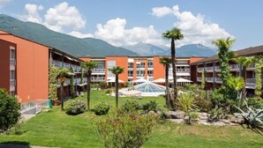 Un hôtel à étages, doté d’espaces extérieurs aménagés pour s’asseoir et d’une cour centrale avec des palmiers et une structure en verre.