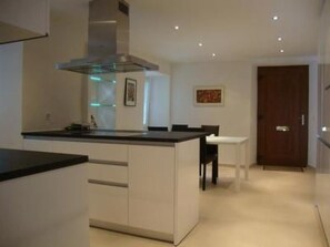 Une cuisine moderne avec un îlot central, un coin repas comprenant une table et des chaises, et une porte en bois à l’arrière-plan.