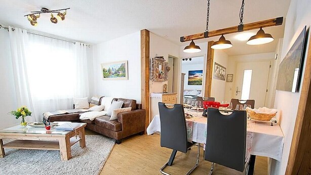 Een moderne woonkamer met een bank, salontafel en een eethoek met stoelen en een tafel.