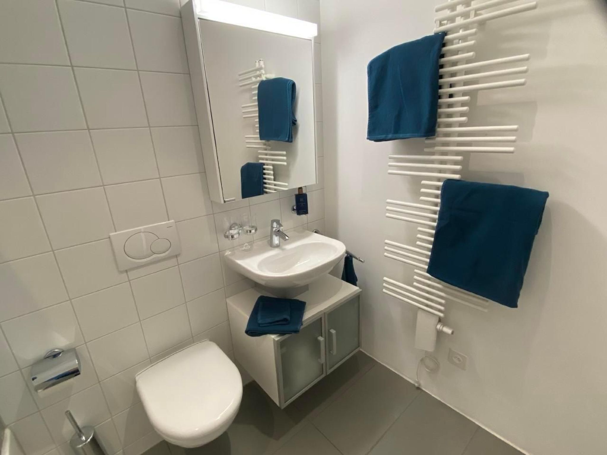 A modern bathroom with a white sink, a toilet, and a mirror. There are two blue towels hanging on a towel rack.
