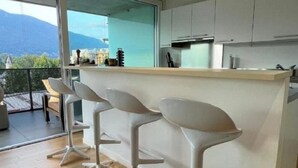 A modern kitchen with a central island and three white bar stools. - Wohnung Orizia by Interhome (Locarno)