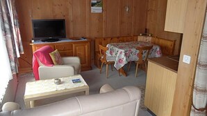 A compact cabin interior with a sofa, a small table, a television, and a dining table with chairs. - Des Alpes 4-Bettwohnung by Interhome (Hasliberg)