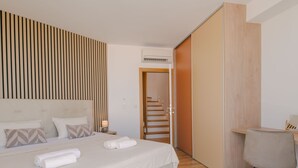 Une chambre moderne avec un grand lit, une tête de lit en bois, un bureau avec une chaise et un escalier menant à une autre pièce.