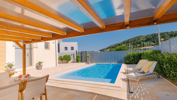 Une piscine surmontée d’une pergola, une table avec des chaises et une vue sur une colline.