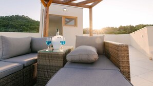 Une terrasse sur le toit, agrémentée d’une pergola en bois, de meubles en osier et d’une table avec une bouteille et des verres.