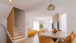 Un intérieur moderne avec un escalier en bois, un coin repas avec une table et des chaises en bois, et un espace de vie comprenant un canapé et une plante.