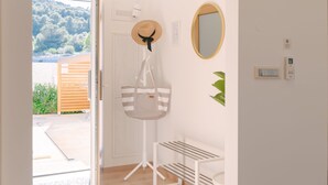 Une pièce avec une porte en bois, un chapeau suspendu, un sac à rayures, un miroir, une plante et un thermostat fixé au mur.