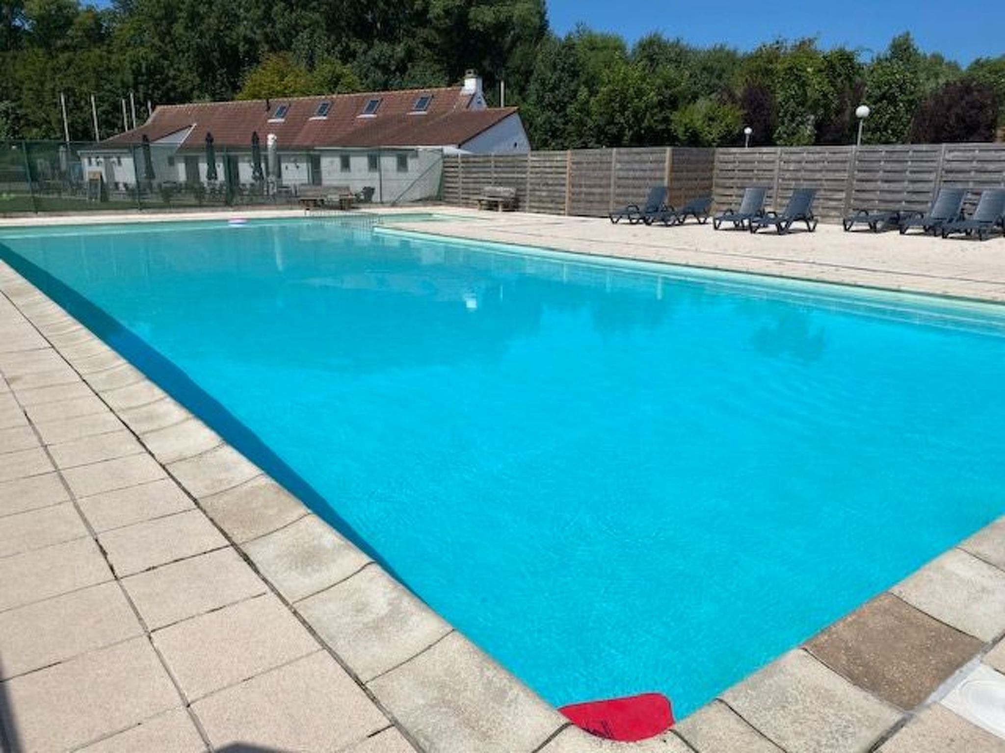 A swimming pool with clear blue water, surrounded by a tiled deck and a wooden fence.